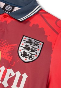 Rotes Poloshirt mit Marinekragen, ausgestattet mit einem silbernen Schildpatch, das schwarze Leoparden und rote Sterne zeigt, sowie fettem weißen Text auf der Vorderseite.