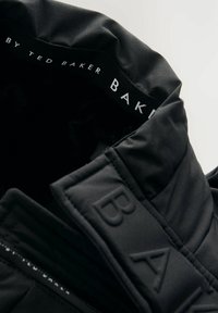 Col en veste matelassée noir avec "BAKER" embossé sur le tissu et "BY TED BAKER" imprimé à l'intérieur du col.