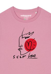 Roze katoenen T-shirt met een grafisch ontwerp van een gezicht en een hart, met de tekst "SELF LOVE" in zwart onder de illustratie.