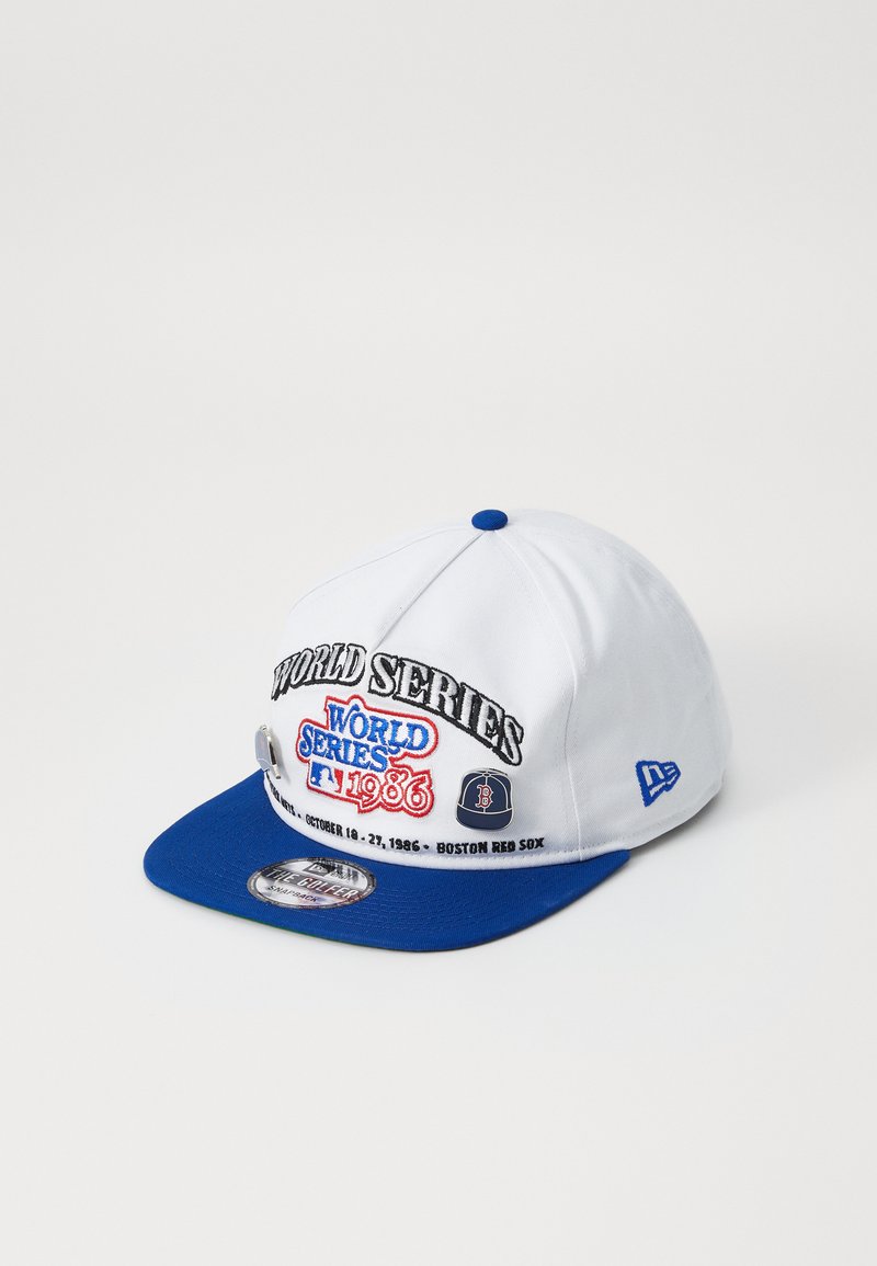 Balta beisbola cepure ar zilu vizieri, ar izšūtu tekstu "WORLD SERIES 1986" un Boston Red Sox detaļām. Izgatavota no auduma ar strukturētu dizainu.