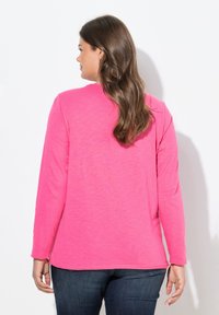 Långärmad topp i klar rosa, tillverkad av mjukt tyg med en avslappnad passform. Har rundad halsringning och något rundad nederkant.