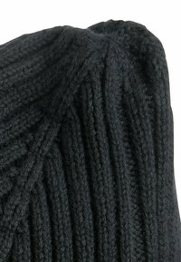 Zwarte gebreide beanie met een geribbelde textuur, voorzien van verticale lijnen en een lichtjes hangende top, gemaakt van zacht wolmateriaal.