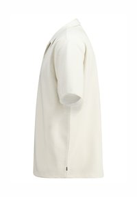 Lyhyttä hihaista polo-paitaa off-white-värissä, jossa on teksturoitu neulekangas, kaulus ja sivuaukot liikkuvuuden helpottamiseksi.