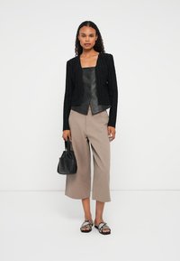 Sort, struktureret cardigan over en tætsiddende sort lædertop; lys beige vide bukser; lille sort taske; sandaler med metalliske detaljer.