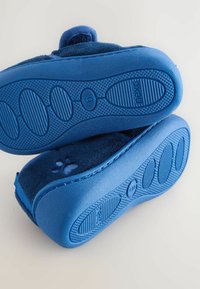 Blaue Hausschuhe mit weichem Obermaterial und rutschfesten Gummisohlen. Mit abgerundeten Kanten und Pfotenabdruckdetails auf dem Obermaterial.