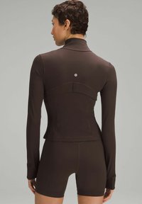 Mørkebrun langærmet atletisk top med en tætsiddende design, høj krave og subtil tonal syning, sammen med matchende shorts.