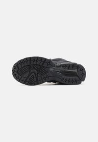 Semelle noire de sneaker avec des motifs de bande de roulement profonds conçus pour l'adhérence et la durabilité, montrée de dessous sur un fond blanc uni.