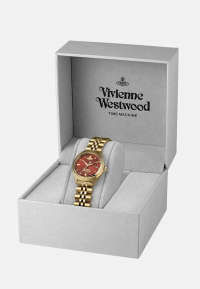 Reloj de oro con una esfera roja en una caja gris, que presenta una pulsera de metal con patrón y el nombre de la marca "Vivienne Westwood" en la esfera.