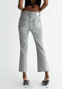 Szare dzwony z denimu, charakteryzujące się wysokim stanem, tylnymi kieszeniami i surowymi brzegami. Tkanina ma subtelna strukturę.