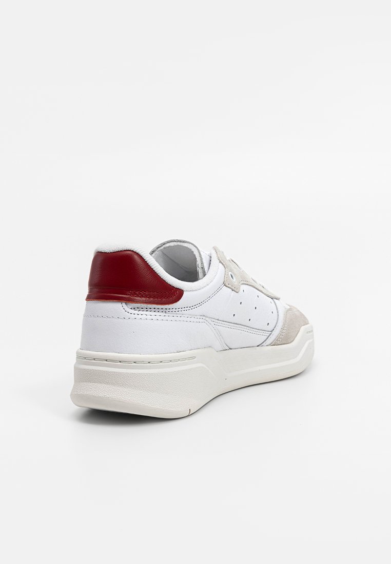 Zapatillas de cuero blancas con acento rojo en el talón, puntera de ante gris y detalles perforados. Suela gruesa con un acabado texturizado. Vista trasera.