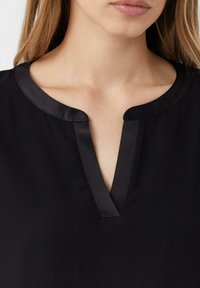 Czarny top z satynowym kołnierzykiem; ma dekolt w kształcie litery V i gładką teksturę. Tkanina wydaje się lekka i ma delikatny połysk.