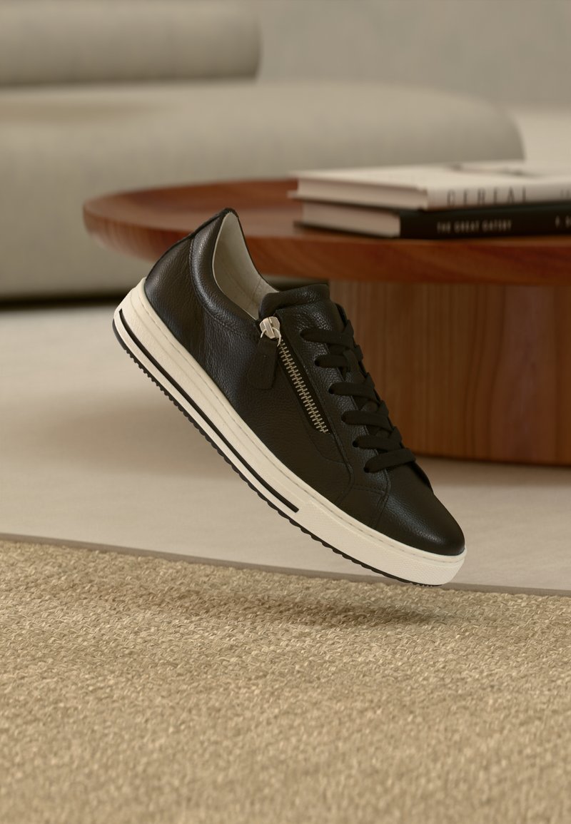 Μαύρο δερμάτινο αθλητικό παπούτσι με λευκή σόλα, διαθέτει μπροστινό κορδόνι και φερμουάρ, υφή στο πάνω μέρος και μινιμαλιστικό σχεδιασμό.