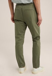 Pantalones de algodón verde oliva con un corte ajustado, que presentan dos bolsillos traseros y un pequeño detalle de logo. Combinados con zapatillas de color claro.