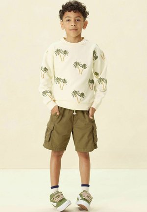Crème sweatshirt met een groen en geel palmbomenpatroon, gecombineerd met olijfgroene cargoshorts. Groene en witte sneakers met roze veters.