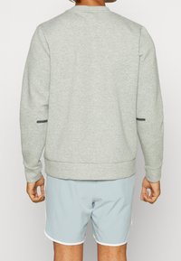 Light gray sweatshirt with a round neck, ribbed cuffs, and hem. Features two side pockets with black accents. Paired with light blue shorts.