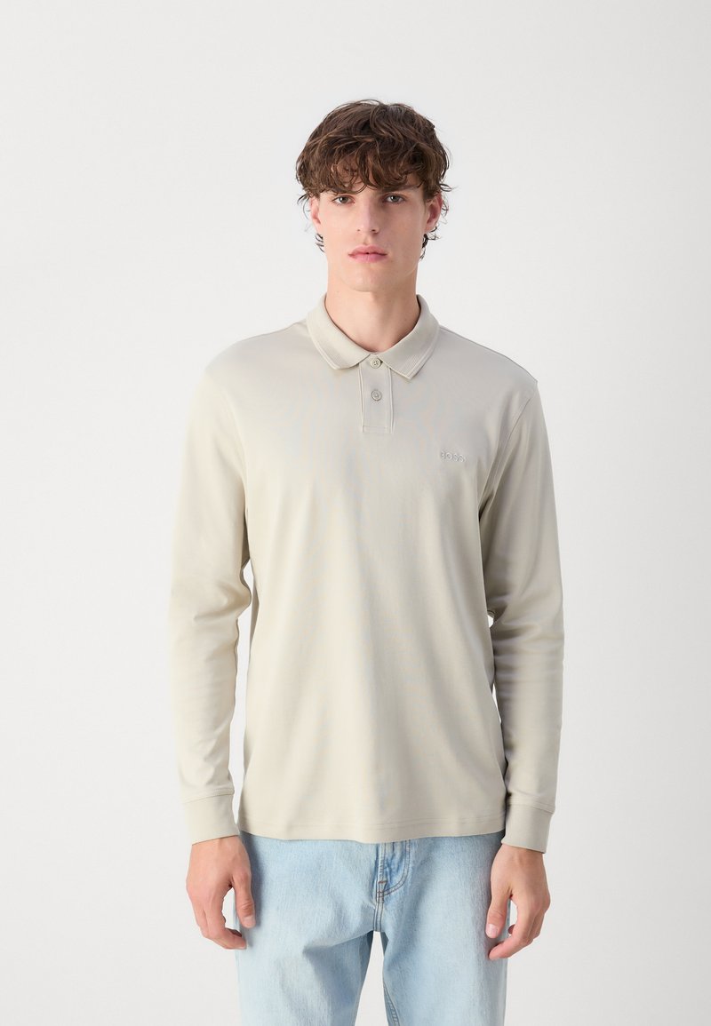 Polo shirt beige clair à manches longues avec un col classique et patte de boutonnage à deux boutons ; comporte un logo brodé subtil sur la poitrine.