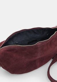 Vīna sarkana zamšveida soma ar rāvējslēdzēju, ar melnu iekšējo odere un iekšējo rāvējslēdzēja kabatu papildu organizācijai.