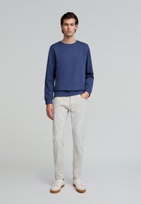 Dunkelblaues Baumwoll-Sweatshirt mit langen Ärmeln, Rundhalsausschnitt und geripptem Saum. Kombiniert mit hellbeigen Chinos und weißen Sneakern.