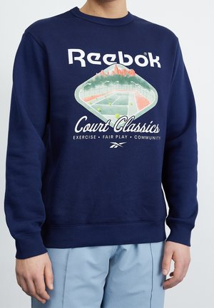 Granatowy sweatshirt z graficznym wzorem przedstawiającym kort tenisowy oraz logo Reebok. Materiał jest gładki, z prążkowanymi mankietami i dołem.