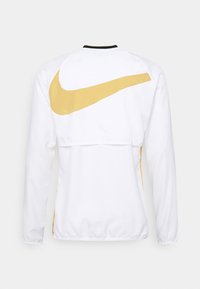 Veste de sport blanche à manches longues avec un grand logo Nike Swoosh doré sur le haut du dos et un col bordé de noir.