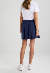 Marinblå plisserad kjol av lättviktig tyg, med resårmidja och en slät yta, ihop med en vit T-shirt och vita sneakers.