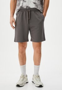 Graue Baumwollmischung-Shorts mit elastischem Bund und Kordelzug, seitlichen Taschen und lockerer Passform, kombiniert mit weißen Socken und Turnschuhen.