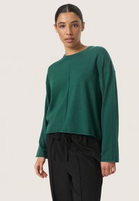 Groene langetermijncroptrui met een ronde halslijn en een gladde textuur, gecombineerd met zwarte broek met trekkoord.