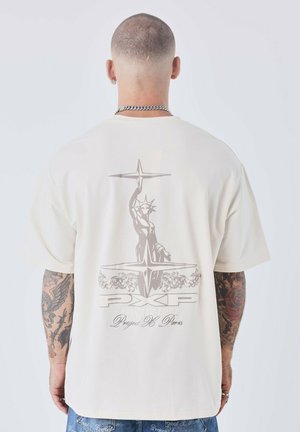 Camiseta de manga corta color crema con un gráfico en gris de la Estatua de la Libertad y texto en la parte posterior, confección en tejido suave y ligero.