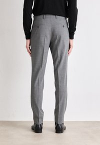 Pantaloni grigi, texture, con una vestibilità slim, caratterizzati da una piega frontale e due tasche posteriori, abbinati a scarpe nere.