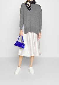 Grauer Strickpullover, weiße Satin-Midi-Rock, weiße Sneakers und eine blaue Handtasche. Schal mit schwarz-weißem Muster um den Hals.
