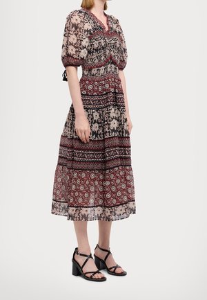 Woman wearing a midi floral print dress with puff sleeves and black heeled sandals with ankle straps, standing sideways.