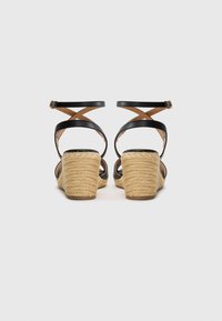 Black leather wedge sandals featuring braided jute heels, cross strap design, and adjustable ankle buckle. Smooth texture with a natural finish.