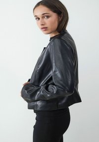 Czarna skórzana kurtka z zarysowanym wzorem, gładką teksturą i dopasowanym krojem. Posiada minimalną ilość elementów metalowych oraz lekko skróconą długość.