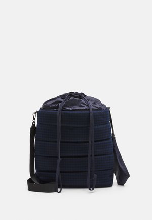 Granatowy worek ze sznurkiem, z pikowaną fakturą, w kratkę, z regulowanym paskiem, miękką tkaniną i kompaktowym cylindrycznym kształtem.