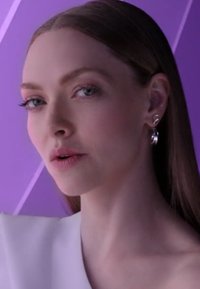 Close-up van een model met lang, steil haar, dat een wit topje draagt. Opvallende kenmerken zijn zilveren oorbellen en een gladde, lichte huid.