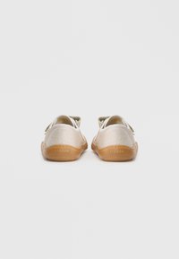 Light gold canvas shoes with a textured upper, white laces, and a flexible brown rubber sole. Features minimal branding on the heel.