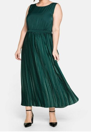 Groene geplooide maxi-jurk met een ronde halslijn, getailleerde taille en een vloeiende rok. Zwarte enkellaarsjes met enkelbandje maken de look compleet.