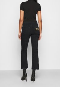 Svarta jeans med vida ben och fransar i fållen, med en bakficka som har logotypdetaljer. Kombineras med svarta högklackade stövlar och en figurnära svart topp.