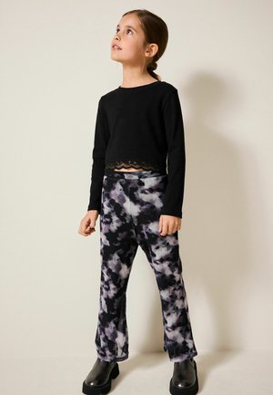 Haut noir à manches longues avec finitions en dentelle, associé à un pantalon à motifs abstraits violet et gris. Modèle portant des bottes à plateforme noires.