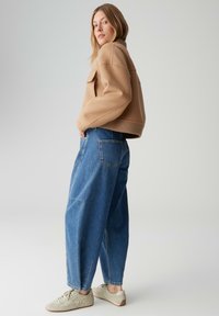 Pull court beige en laine mélangée avec épaules tombantes, associé à un jean denim bleu surdimensionné et des baskets gris clair.