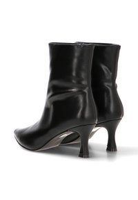 Par de botas de tobillo de cuero negro con tacones bajos y puntas afiladas, exhibidas sobre un fondo blanco.