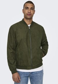 Giacca bomber verde oliva in materiale simil-suede. Presenta una cerniera frontale, polsini a costine e una vestibilità morbida. Design complessivamente minimalista.