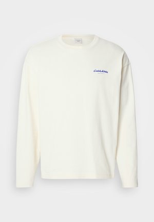 Pikad varrukad, kreemivärvi t-särk, mis on valmistatud puuvillast, ümarate kaelustega, vasakul rinnaalal on väike sinine Calvin Kleini logo. Pehme tekstuur.