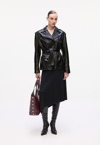 Black leather motorcycle jacket with a belted waist, paired with a dark asymmetrical skirt and knee-high black boots. Burgundy tote bag with silver studs.