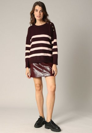 Pull rayé bordeaux avec des lignes horizontales roses, présentant des accents de boutons à l'épaule. Associé à une mini jupe bordeaux brillante et des chaussures noires.