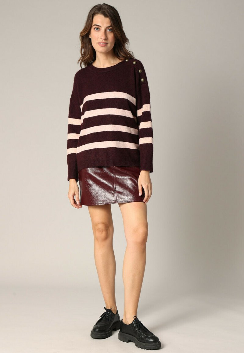 Pull rayé bordeaux avec des lignes horizontales roses, présentant des accents de boutons à l'épaule. Associé à une mini jupe bordeaux brillante et des chaussures noires.