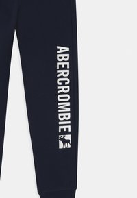 Navy blue sweatpants leg with white vertical "ABERCROMBIE" text and a moose logo near the ankle.
