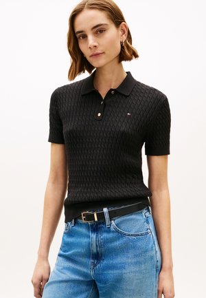 Tricou polo negru cu textură, cu guler, butoane aurii și un logo mic. Asortat cu blugi din denim albastru deschis și o curea neagră.