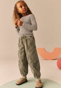 Gestreiftes Langarm-Oberteil kombiniert mit einer grünen Cordhose mit elastischem Bund, seitlichen Taschen und elastischen Bündchen, dazu braune Slipper.