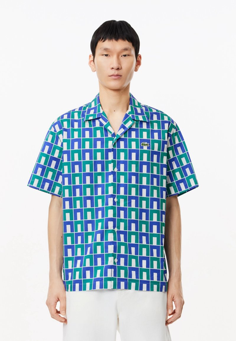 Chemise à manches courtes avec un motif géométrique vert, bleu et blanc. Comprend un col et un petit logo brodé.
